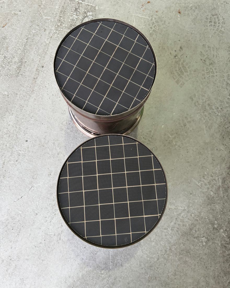Two cleaned diesel particulate filters stood on end on a workshop floor, viewed from above, showing the open ceramic cell matrix and the pale cement joins between substrate segments.