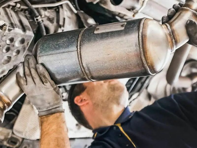 A technician working under a raised vehicle, guiding a diesel particulate filter out of the exhaust line.